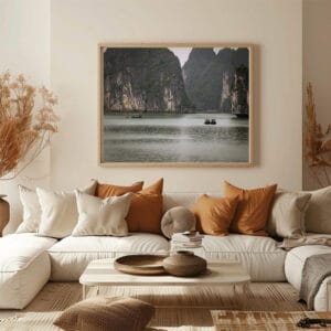 A natural frame with a photo of 2 fishing boats in Halong bay hanged above a beige sofa with beige and brown pillows. In front a low coffee table