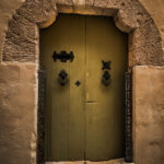 A green door with a metal handle set within a stone archway in Mdina, showcasing classic architectural details.