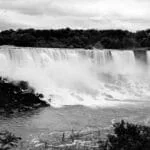 Monochrome depiction of Niagara Falls, highlighting the dramatic flow of water and surrounding natural beauty.