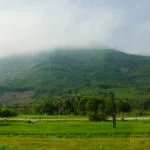 A distant mountain shrouded in fog, set against the serene hills of the Vietnamese countryside