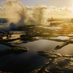 a large wave hitting the coastline during sunrise at Marsascala coastline near salt pans reflecting