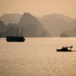 boats silhouttes in Halong bay during sunset with mountain layers in the background