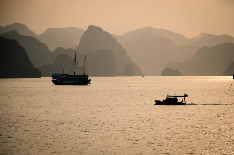 boats silhouttes in Halong bay during sunset with mountain layers in the background