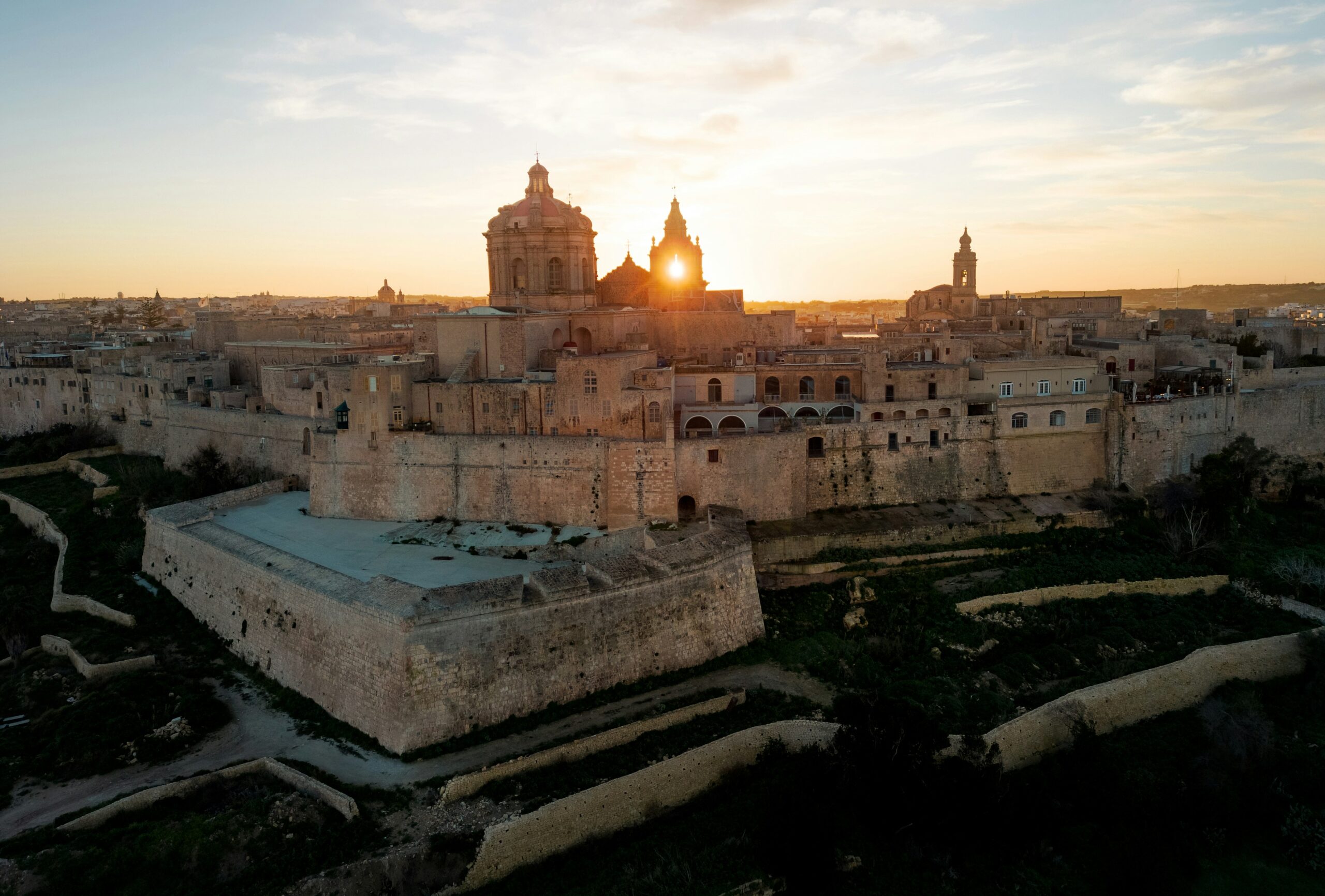 Aerial view of Mdina City, Malta, as the sun sets, casting a warm glow over the historic cityscape.