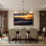 Classic dining room with long wooden table, upholstered chairs, and a large framed sunset seascape on the wall.