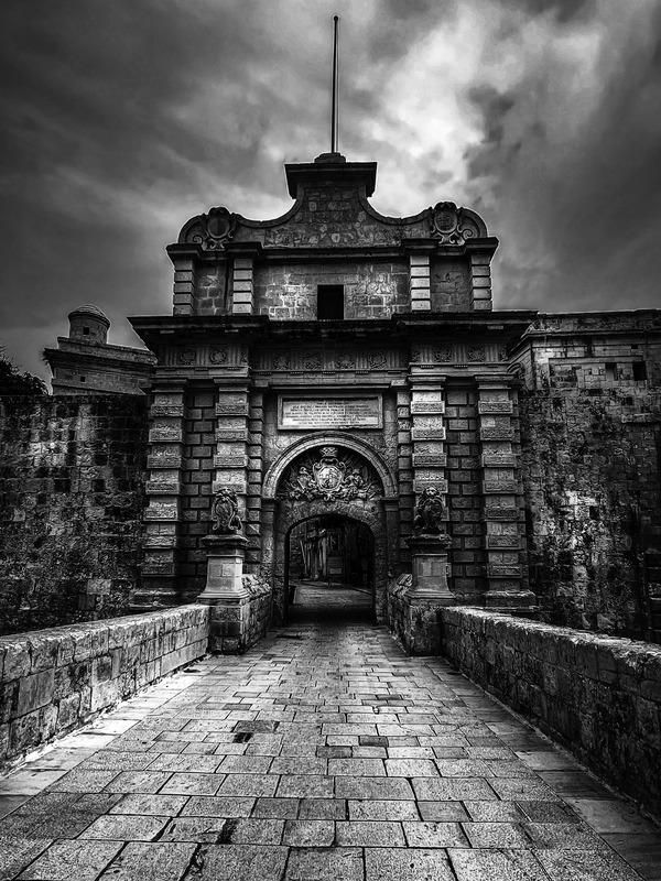 beautiful stone archway of Mdina Gate in Black and White, with a clock tower visible in the background, blending history and charm