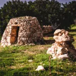 A Maltese Girna, a traditional stone building, featuring a rustic door, set against a natural landscape.