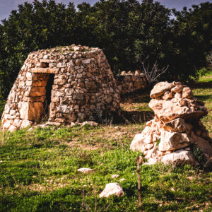 A Maltese Girna, a traditional stone building, featuring a rustic door, set against a natural landscape.