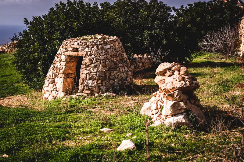 A Maltese Girna, a traditional stone building, featuring a rustic door, set against a natural landscape.