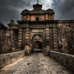 beautiful stone archway of Mdina Gate, with a clock tower visible in the background, blending history and charm