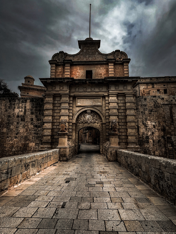 beautiful stone archway of Mdina Gate, with a clock tower visible in the background, blending history and charm