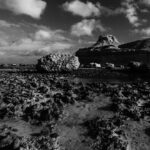 Monochrome photograph of rugged rocks and tranquil water at Gozo Qbajjar, highlighting the serene coastal landscape.