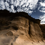 Eroded rock formations with textured layers under a sky filled with scattered clouds at Gozo Qbajjar