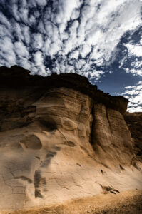 Eroded rock formations with textured layers under a sky filled with scattered clouds at Gozo Qbajjar