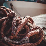 A heap of rope is positioned on the ground adjacent to a fishing boat in Valletta Harbour, reflecting local fishing culture.