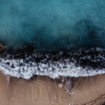 Aerial image capturing the Gozo beach, with waves rolling in from the ocean, creating a picturesque coastal scene.