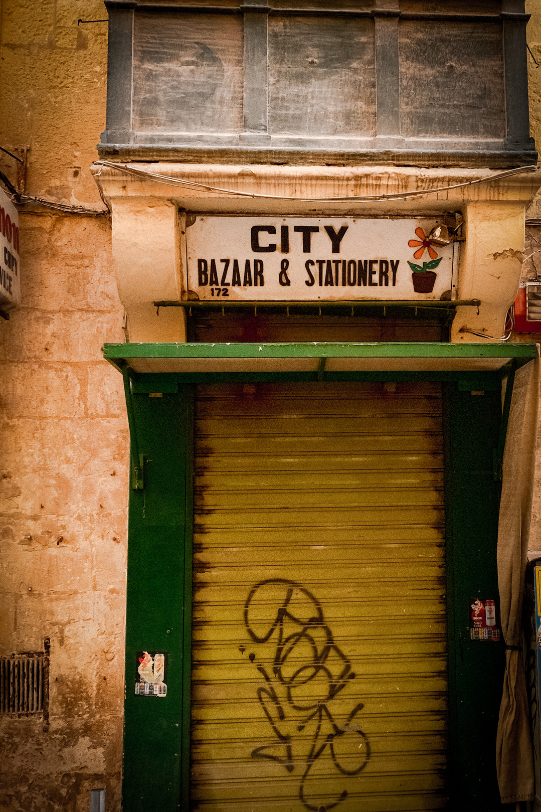 A vibrant green door featuring graffiti that says "city," situated at a historic stationery shop in Valletta's bazaar.