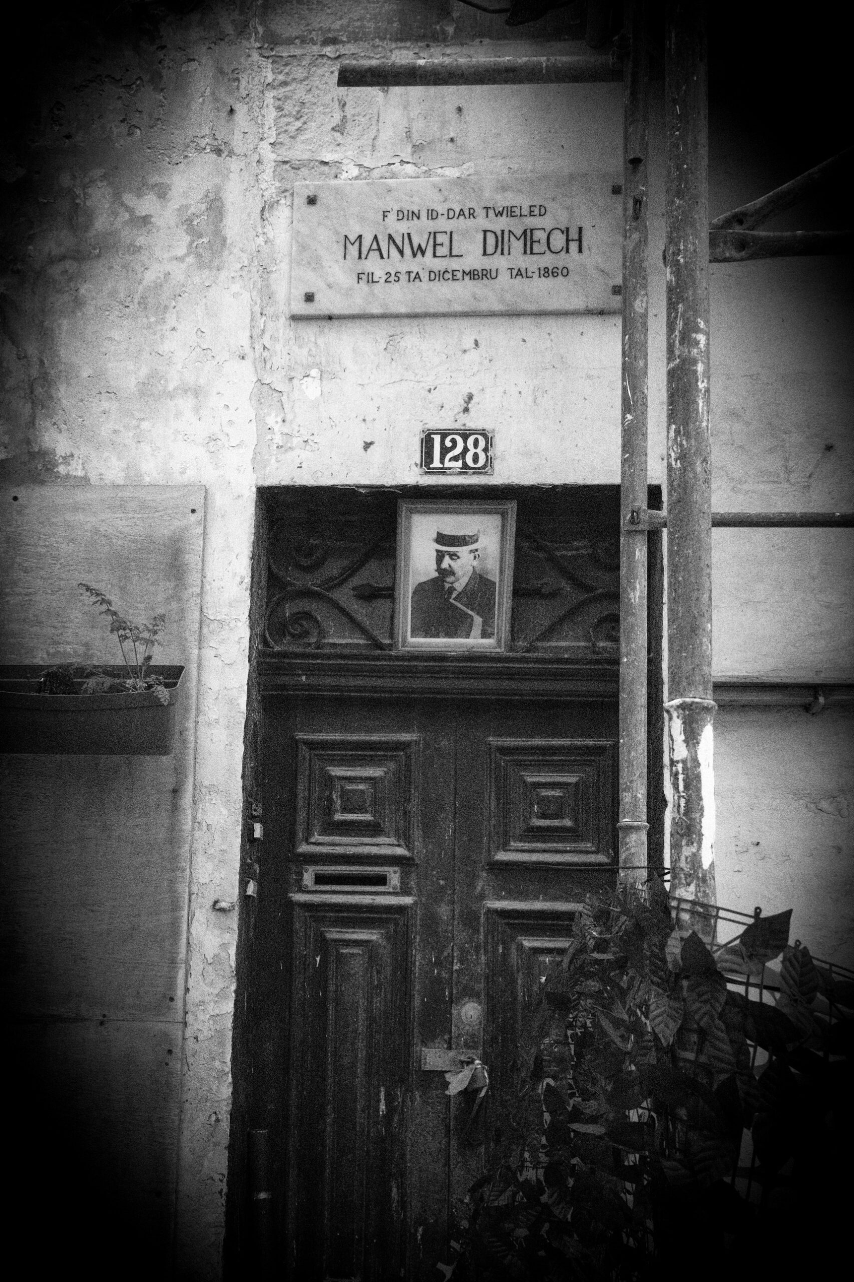 A black and white image of a door with a sign, representing the birthplace of Manuel Dimech