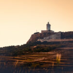 Lighthouse on a hilltop at sunset surrounded by terraced fields in Gozo.