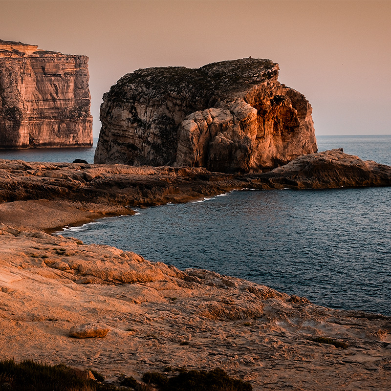 Fungus Rock at sunset in Dwejra Bay, Gozo, with warm cliffs and calm sea.