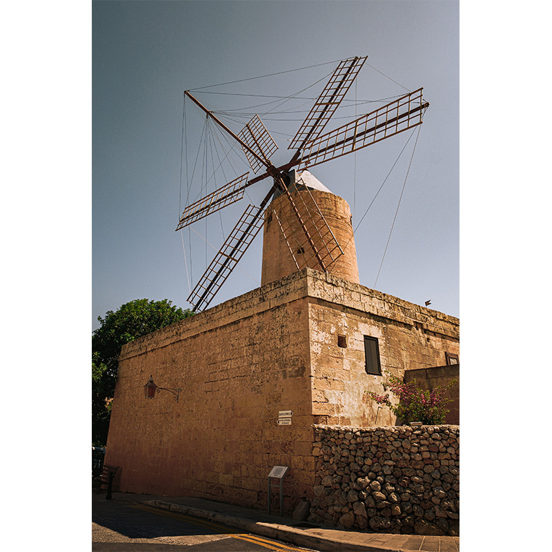 Historic stone windmill in Gozo, Malta, under warm sunlight with clear blue sky.