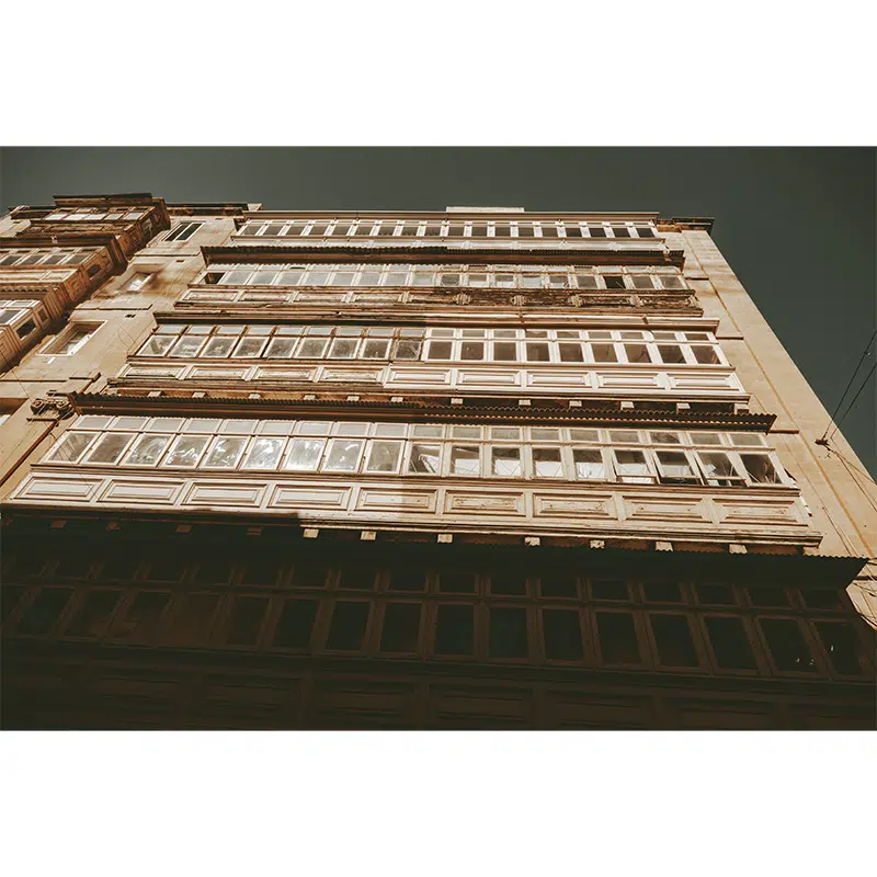 Wide view of a grand historical Valletta building with many enclosed balconies.