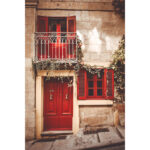 Red door, balcony, and window with green ivy on a limestone Valletta house.