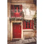 Red door, balcony, and window with green ivy on a limestone Valletta house.
