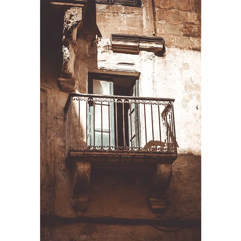 Sunlit vintage stone balcony with open green shutters in Valletta.