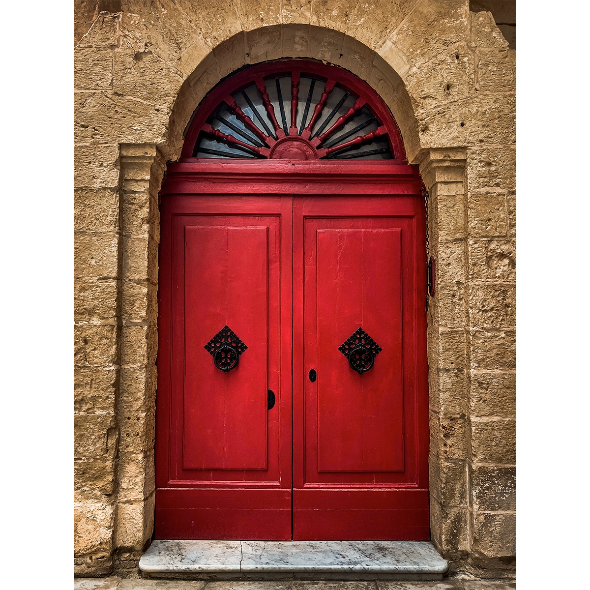 Red traditional Maltese door in stone archway in Mdina