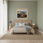 A person stands on the reddish-orange sands of Ramla Bay in Gozo, Malta, looking out at the calm, turquoise Mediterranean sea. The iconic Ramla Rocks, large geological formations, rise majestically from the water in the middle ground under a clear blue sky.