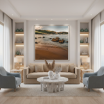 A person in a sun hat is walking along the sandy Ramla Bay shoreline in Gozo, with turquoise water reaching the shore and limestone cliffs in the background under a blue sky.