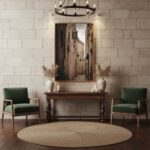 A white modern living room with a large window overlooking a garden, featuring a Malta Mdina Lantern Alley canvas print hung above a light grey sofa with throw pillows and a beige blanket, a round coffee table with books and a candle, a floor lamp, and a potted plant.