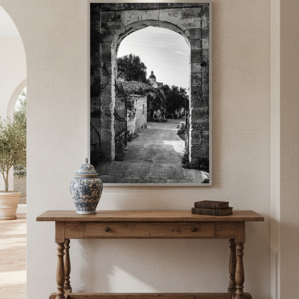 A stunning view through a rustic stone archway of the Mtahleb Church in Malta, bathed in warm sunset light. The archway frames a dramatic landscape with rolling hills and the Mediterranean sea in the distance under a golden sky.