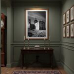 A framed print of Malta Mtahleb Church hanging on a white wall above a wooden side table with a green plant in a white pot, a stack of books, and a cup of coffee, creating a minimalist and serene living space.