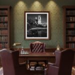 A serene living room with a large window overlooking a natural landscape, showcasing the "Malta Mtahleb Church Reflection - Malta Wall Art" print hanging prominently on a light grey wall above a modern, light-colored sofa. The artwork captures a beautiful reflection of the Mtahleb Church, creating a focal point in the minimalist decor.