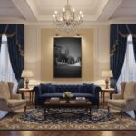 A beautifully decorated living room with a large window overlooking a picturesque view of St. Paul's Church in Rabat, Malta. The room features a comfortable sofa, a coffee table with books, and a vibrant green plant. On the wall above the sofa, a framed 'Rabat Malta Zuntier St. Pauls Church View - Wall Art' print is displayed, enhancing the room's aesthetic.