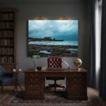 A person in a casual outfit sits on a rocky beach at dusk, holding a blue-colored portable power bank, with the serene Mediterranean Sea and a faint horizon in the background, conveying a sense of adventure and utility.