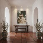 A person holding a travel-sized tube of "Malta Marsaxlokk Parish Church" sunscreen in front of a sunny beach scene with a church in the background, suggesting travel and sun protection.