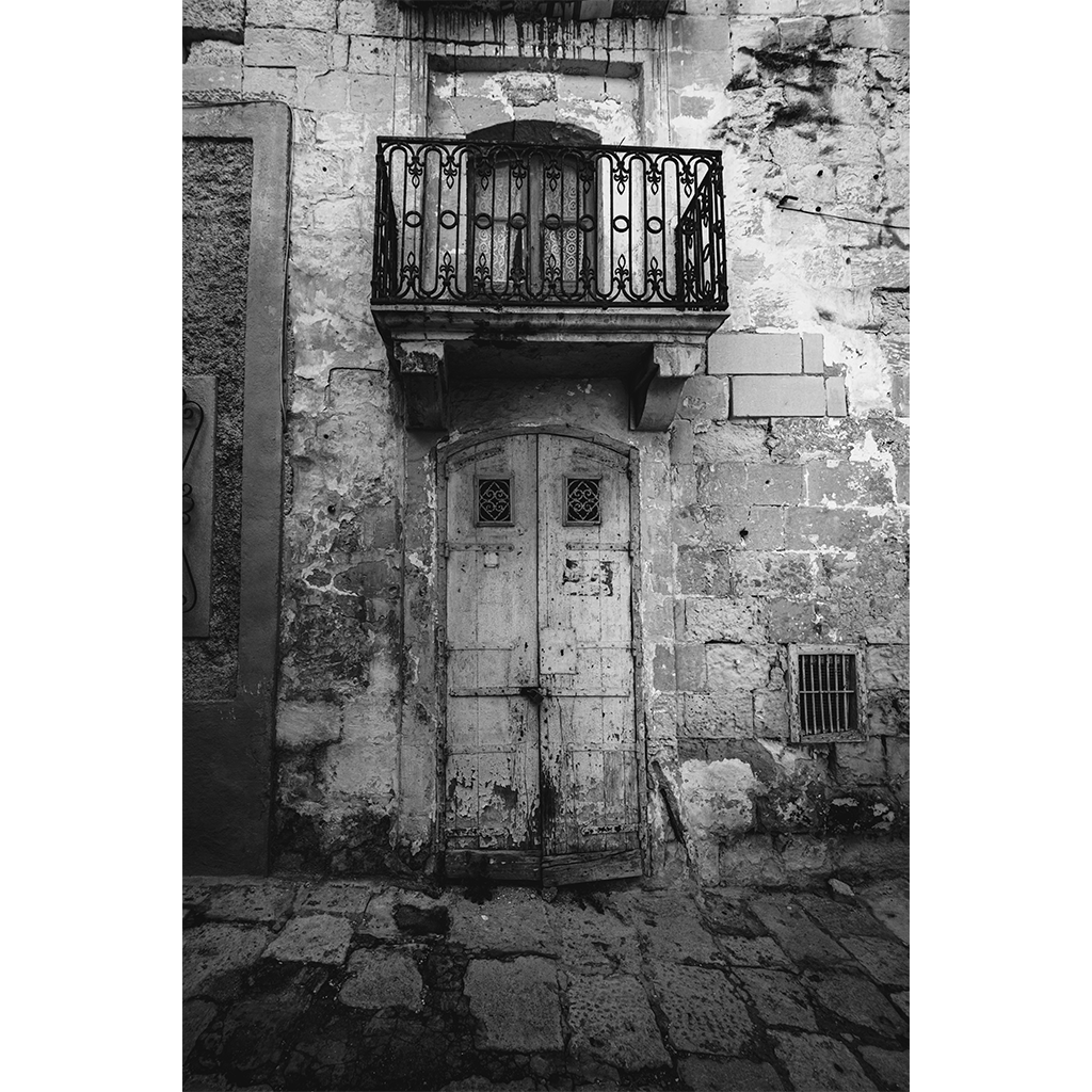 Weathered wooden door beneath wrought iron balcony