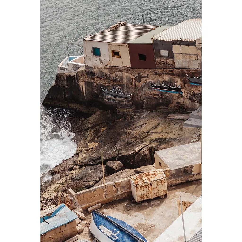 Weathered seaside buildings on rocky cliff above waves