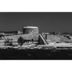 Historic stone fort beside water in black and white