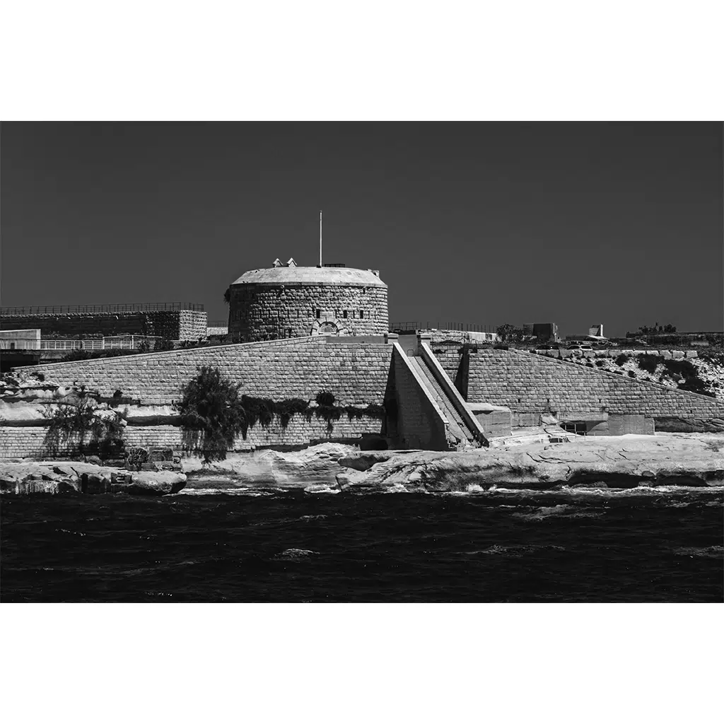 Historic stone fort beside water in black and white