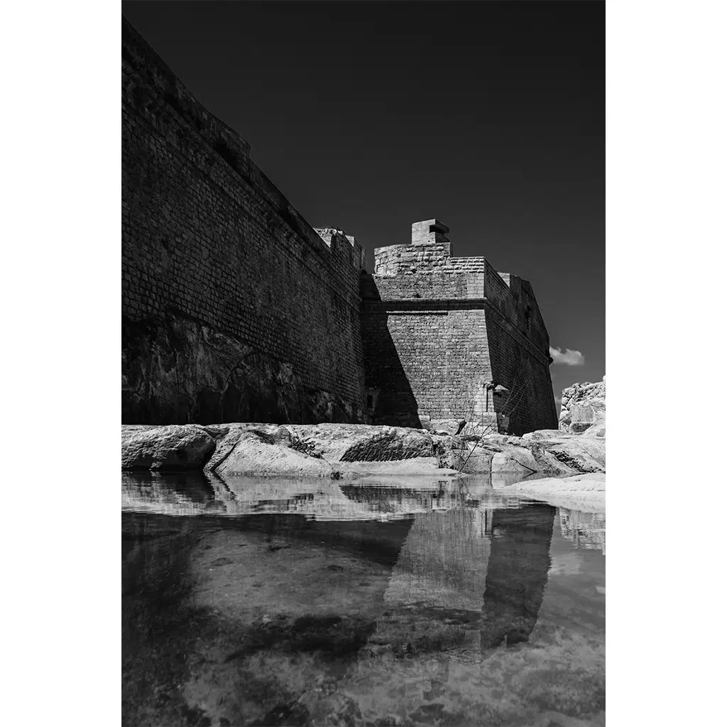 Stone fortress wall reflected in calm water