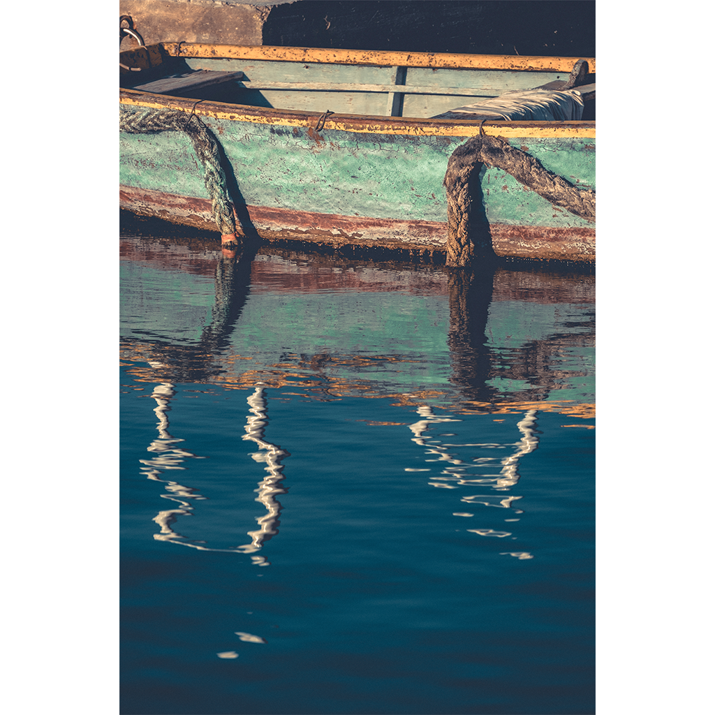 Weathered turquoise boat with ropes reflected in calm water