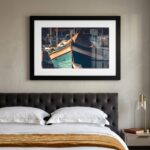 Framed boat photograph above tufted bed
