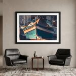Framed turquoise boat photograph above black lounge chairs