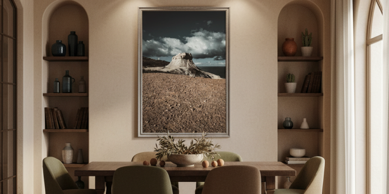 A person gazes at the "Gozo Qbajjar Qolla Bajda Dusk" print, which hangs on a sun-drenched living room wall, with a monstera plant in the foreground.